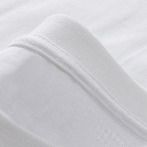Może przedstawiać: Zbliżenie białego kołnierzyka koszulki. Kołnierz jest prążkowany i złożony, ukazując szwy i fakturę materiału. Tkanina wydaje się być miękkim, lekkim materiałem.