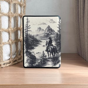 Puede incluir: Una ilustraci&oacute;n en blanco y negro de una persona a caballo cabalgando por un paisaje monta&ntilde;oso. La persona lleva un sombrero de vaquero y el caballo est&aacute; de espaldas al espectador. El fondo es una cordillera con un lago en primer plano.