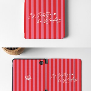May include: A red and pink striped Kobo e-reader case with the text "I'd Rather be Reading" and a small heart. The case is closed and the front cover is visible.