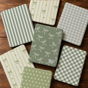 May include: A collection of six rectangular cases featuring various sage green and white patterns including vertical stripes, gingham checks, small polka dots, and scattered ribbon motifs. One central case displays the script text Thida.
