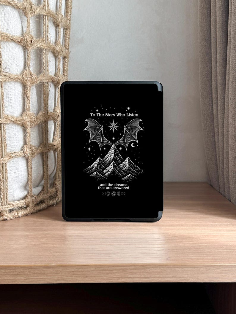 K&ouml;nnte beinhalten: Schwarze Tablet-H&uuml;lle mit einer wei&szlig;en Grafik, die Berge, Sterne und ein fledermausartiges Fl&uuml;geldesign zeigt. Der Text lautet "To The Stars Who Listen" und "and the dreams that are answered."