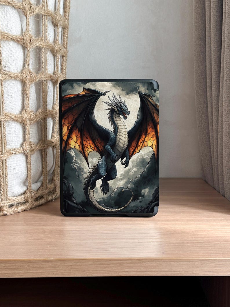 May include: A black case featuring a detailed illustration of a dragon with black and orange wings, soaring against a cloudy sky. The dragon has a blue body and a long tail. The case is displayed on a wooden surface.