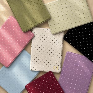 May include: A collection of eight rectangular e-reader covers featuring a polka dot pattern in various colors including olive green, light green, pink, black, cream, light blue, dark red, and purple. The cream cover features the gold letters ST.