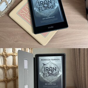 Peut inclure: Une liseuse Kindle noire avec un &eacute;tui gris. L'&eacute;cran affiche la couverture du livre "Iron Flame" de Rebecca Yarros. La couverture du livre pr&eacute;sente un design circulaire avec les mots "Iron Flame" dans une police de caract&egrave;res stylis&eacute;e. Le texte "EEN IJZEREN VLAM" est &eacute;galement visible sur la couverture.