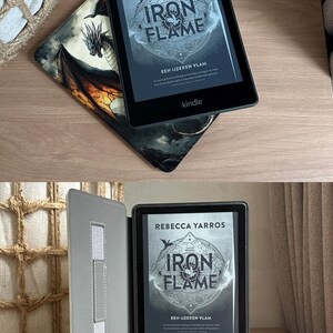 May include: A black Kindle e-reader displaying the book "Iron Flame" by Rebecca Yarros. The cover features a stylized design with the title in large letters. The e-reader rests on a decorative case with a dragon illustration.