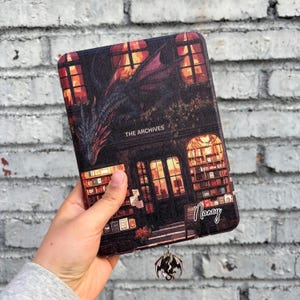 May include: A book cover featuring a black and red dragon design with the text "The Archives" and a name "Nancy" written on the bottom right corner. The cover is made of a textured material and has a silver dragon bookmark.