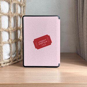vintage and vibrant Kindle case featuring a soft pink background with three bold red ticket-style designs labeled “LATENIGHT BOOK CLUB” and marked “SINGLE USE.” Decorative pink hearts and sparkles add a whimsical, cozy vibe—perfect for book lovers who enjoy getting lost in stories after dark.