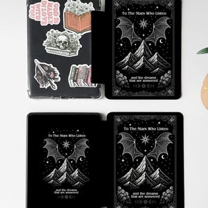 K&ouml;nnte beinhalten: Schwarze Tablet-H&uuml;lle mit doppelseitigem Design. Eine Seite zeigt eine detaillierte Illustration mit Bergen, Sternen und dem Text "To The Stars Who Listen". Die andere Seite hat Aufkleber mit verschiedenen Designs. Die H&uuml;lle hat einen integrierten Riemen und eine magnetische R&uuml;ckseite.
