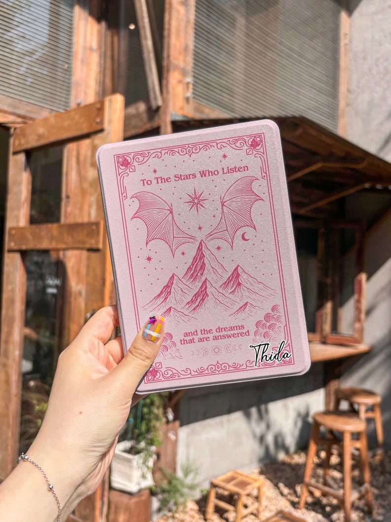 May include: A pink rectangular case with the text "To The Stars Who Listen" and "and the dreams that are answered". The case features a mountain and wing design. The name "Thida" is printed on the bottom right.