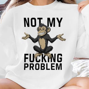 Może przedstawiać: Biała bluza z czarnym i brązowym rysunkiem małpy i tekstem "NOT MY FUCKING PROBLEM".