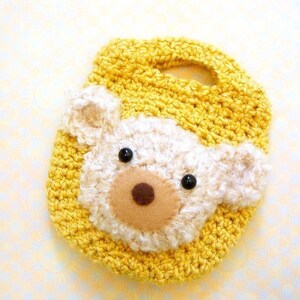 May include: A yellow crocheted phone case with a white crocheted bear face. The bear has black eyes and a brown nose.