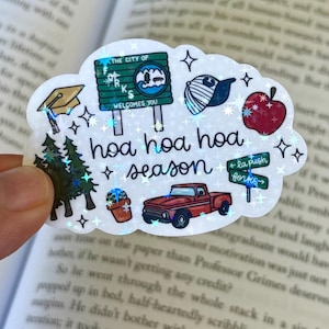 May include: A holographic sticker in the shape of a cloud, featuring various illustrations and the text "hoa hoa hoa season." The sticker includes images of a graduation cap, a truck, and an apple.