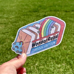May include: A holographic sticker shaped like a toaster pastry with a rainbow arc, white daisy flowers, and a blue patterned corner. The text reads WonderRead CLASSIC EDITION in black lettering against a light blue background with a red border.