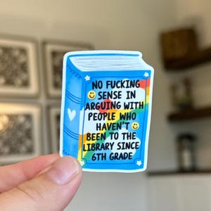 May include: A blue sticker in the shape of a book with the text "NO FUCKING SENSE IN ARGUING WITH PEOPLE WHO HAVEN'T BEEN TO THE LIBRARY SINCE 6TH GRADE." The sticker has a rainbow design and a white heart.