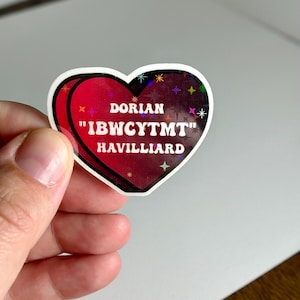 以下が含まれることがあります： ホログラフィック仕上げの赤いハート型のステッカー。ステッカーには、「DORIAN "IBWCYTMT" HAVILLIARD」という白い文字が書かれています。