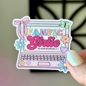 May include: A pink laptop sticker with the words "FANFIC Girlie" in colourful bubble letters. The sticker features a bow, flowers, a butterfly, and a heart. Text at the bottom reads "You already left kudos here :)".