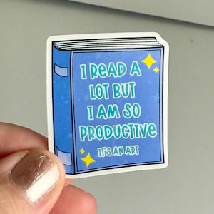 Puede incluir: Una pegatina azul en forma de libro con el texto "Leo mucho pero soy tan productivo que es un arte" con estrellas amarillas.