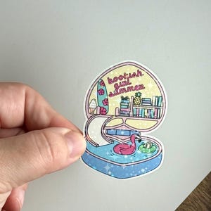 May include: A colorful sticker featuring a whimsical design with the text "bookish girl summer." The sticker depicts a pool with a flamingo float, a bookshelf, and a surfboard with an ice cream cone.