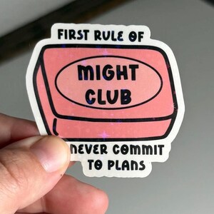 Puede incluir: Una pegatina rosa y blanca con el texto "First rule of Might Club Never commit to plans". La pegatina tiene la forma de una pastilla de jabón.