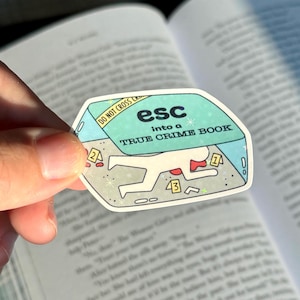 May include: A sticker with a light blue border and the text "esc into a TRUE CRIME BOOK." The sticker features a cartoon illustration of a crime scene with a body outline and evidence markers. The words "DO NOT CROSS" are also visible.