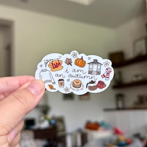 May include: A white die-cut sticker featuring colorful illustrations of a pumpkin, a gazebo, a sweater, a coffee cup, a stack of pancakes, a coffee pot, a mug, and a sign that reads Luke's, with the text i am an autumn written in the center.