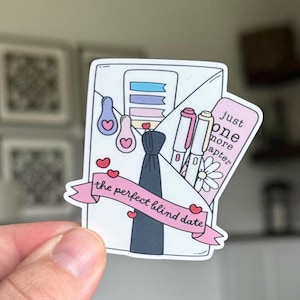 Puede incluir: Una pegatina blanca con una pancarta rosa que dice "the perfect blind date". La pegatina presenta una corbata negra, bolígrafos, corazones y el texto "just one more chapter."