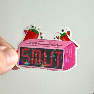 May include: A pink sticker featuring a digital alarm clock with the word "SMUT" displayed in red. Two red chili peppers with green stems and hearts and stars are above the clock.