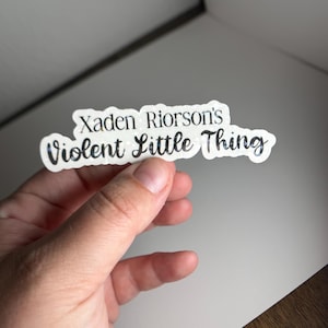 May include: A white sticker with black text that reads "Xaden Riorson's Violent Little Thing".