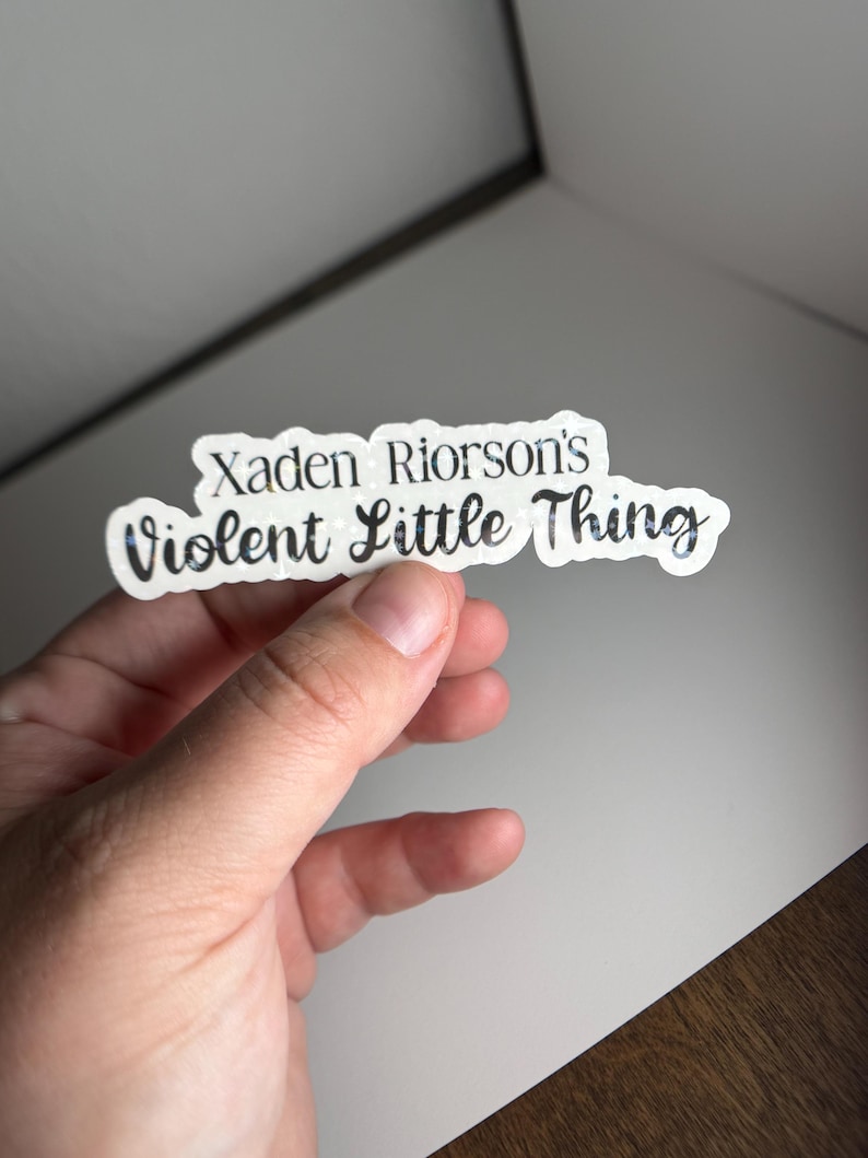 May include: A white sticker with black text that reads "Xaden Riorson's Violent Little Thing".