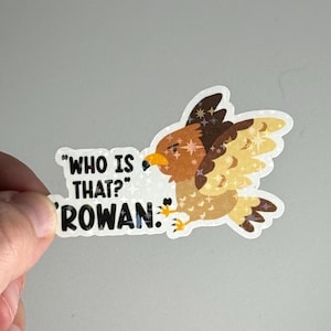 May include: A sticker featuring a cartoon hawk with outstretched wings. The hawk is brown, tan, and yellow with a yellow beak. Text on the sticker reads "WHO IS THAT? ROWAN."