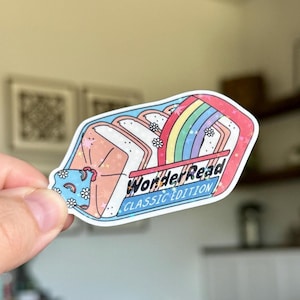 May include: A colorful sticker with a whimsical design. The sticker features a sandwich with a rainbow and the text "WonderRead CLASSIC EDITION". The sticker has a pink, blue, and white color scheme with floral and star accents.