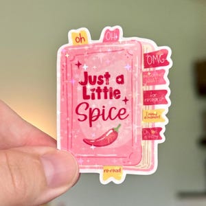 May include: A pink rectangular sticker shaped like a book with the text Just a Little Spice and a red chili pepper illustration. The sticker features holographic star accents and several colorful page tabs with text including oh, OH, OMG, WHAT, and re-read.