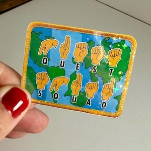 Könnte beinhalten: Ein blauer und grüner Aufkleber mit einem Weltkarten-Design. Der Aufkleber zeigt eine Reihe von Handzeichen, die das Wort "QUEST" in amerikanischer Gebärdensprache buchstabieren. Der Aufkleber hat einen gelben Rand.
