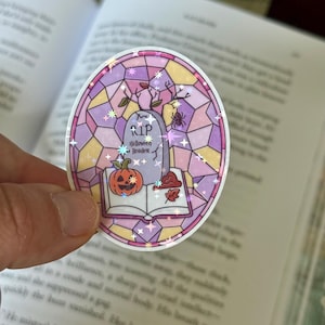 May include: Oval sticker with a stained glass design featuring a tombstone with "RIP Halloween Reader" text, a jack-o'-lantern, and an open book. The sticker has purple, yellow, and pink hues with glitter accents.