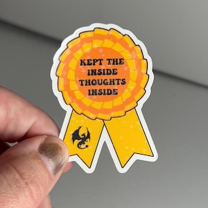 Puede incluir: Una pegatina de cinta amarilla y naranja con el texto "KEPT THE INSIDE THOUGHTS INSIDE" y una silueta negra de un dragón.