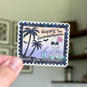 Könnte beinhalten: Aufkleber mit holografischem Rand, der ein Skelett mit einer Blume, Palmen und dem Text "Happy Summerween" und "wish you were here!" zeigt. Der Hintergrund hat einen Farbverlauf aus Lila, Orange und Blau.