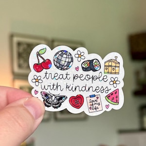 Könnte beinhalten: Ein holografischer Aufkleber mit verschiedenen Illustrationen, darunter Kirschen, eine Discokugel, Sushi und ein Schmetterling. Der Aufkleber trägt den Schriftzug "treat people with kindness" und andere kleine Bilder. Der Aufkleber wird von einer Hand gehalten.