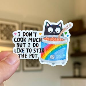 Peut inclure: Autocollant représentant un chat noir remuant une marmite de nourriture. La marmite est ornée d'un arc-en-ciel et d'étoiles. Le texte sur l'autocollant se lit comme suit : « Je ne cuisine pas beaucoup, mais j'aime bien remuer la marmite. »