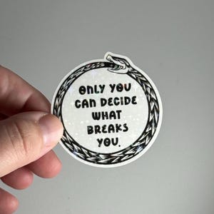 May include: A circular sticker featuring the text "ONLY YOU CAN DECIDE WHAT BREAKS YOU." It has a black and white snake design around the edge and a holographic finish. The snake's head is at the top.