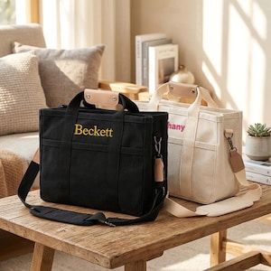 Può includere: Due borse tote rettangolari in tela con tracolle regolabili e manici superiori con dettagli in pelle color cuoio chiaro. La borsa nera mostra il nome Beckett in ricamo giallo, mentre la borsa color crema mostra un nome in testo rosa.