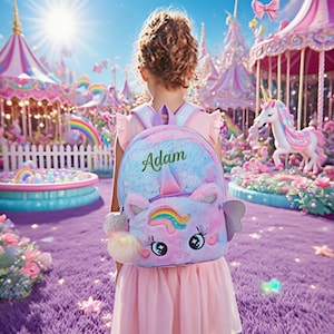 Puede incluir: Una mochila de unicornio de peluche con una melena y cuerno de arcoíris, y el nombre "Adam" bordado en la parte delantera. La mochila es de color azul claro, rosa y morado. La niña lleva un vestido rosa.