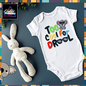 May include: White baby onesie with a gray koala wearing sunglasses and the text "Too Cool For Drool" in colorful letters.