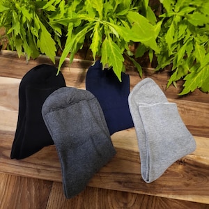 May include: Four pairs of socks in different colors: black, gray, dark gray, and light gray. The socks are folded and arranged on a wooden surface.