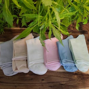 May include: Six pairs of socks in various pastel colors, including light blue, beige, white, pink, and green. The socks are folded and laid out on a wooden surface.