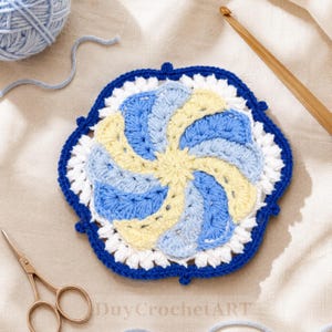 May include: A circular crochet motif featuring a swirling pinwheel pattern in alternating shades of light blue, pale yellow, and white. The design is bordered by a thick, dark blue yarn edge with small decorative picot loops along the perimeter.