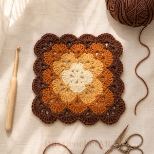 May include: A square crochet motif featuring a scalloped edge in a gradient of cream, golden yellow, burnt orange, and dark brown yarn. A wooden crochet hook lies to the left, while a ball of brown yarn and metal scissors are positioned nearby.
