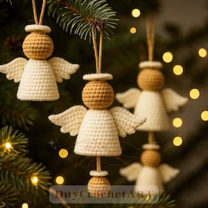 Può includere: Ornamenti a forma di angelo all'uncinetto in crema e marrone, appesi a un ramo di albero di Natale. Gli angeli hanno un'aureola, ali e un piccolo elemento decorativo in basso. L'immagine ha una messa a fuoco morbida con luci bokeh sullo sfondo.