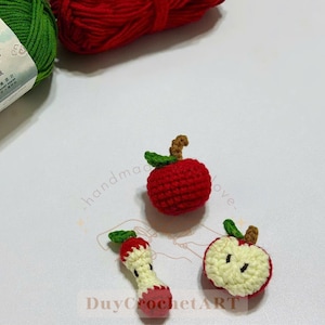 May include: Handmade crochet apple decorations in red, green, and brown. The image shows a whole apple, a half-eaten apple, and an apple core. The text "DuyCrochetART" is visible.