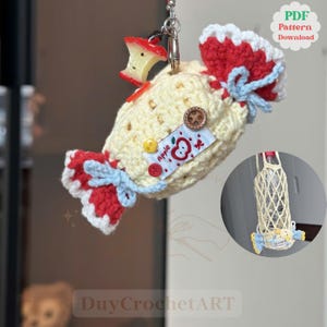 May include: A cream, red, and blue crochet candy-shaped keychain with an apple charm. The keychain has button details and a tag with an apple graphic and the word "Apple". A small bottle holder is also included in the design.
