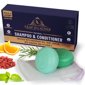 Puede incluir: Dos barras de champú y acondicionador verdes con el logotipo de Leaf & Lather, infundidas con aceite de romero, menta, biotina, ginseng rojo y vitamina C. Las barras están en una bolsa de malla blanca con un cordón de ajuste morado. La imagen también incluye bayas de goji, rodajas de naranja, ramitas de romero y hojas de menta.